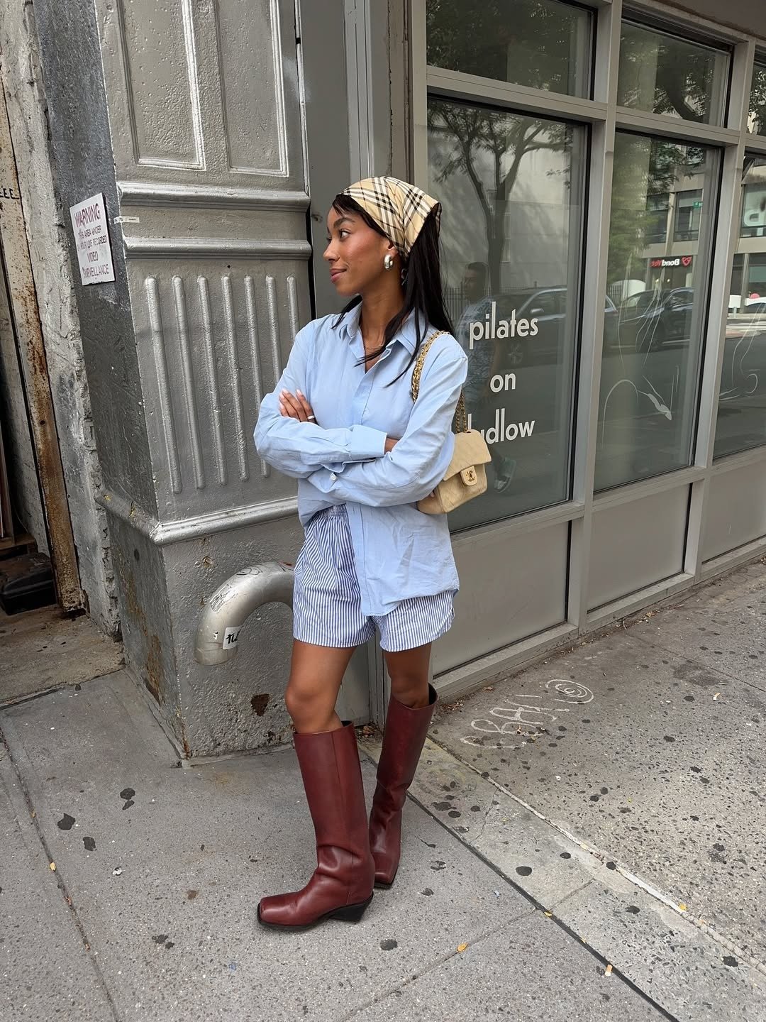 A imagem apresenta uma jovem com um visual contemporâneo, destacando os sapatos tendência 2026: botas altas em tom bordô, que trazem um ar de sofisticação e estilo.