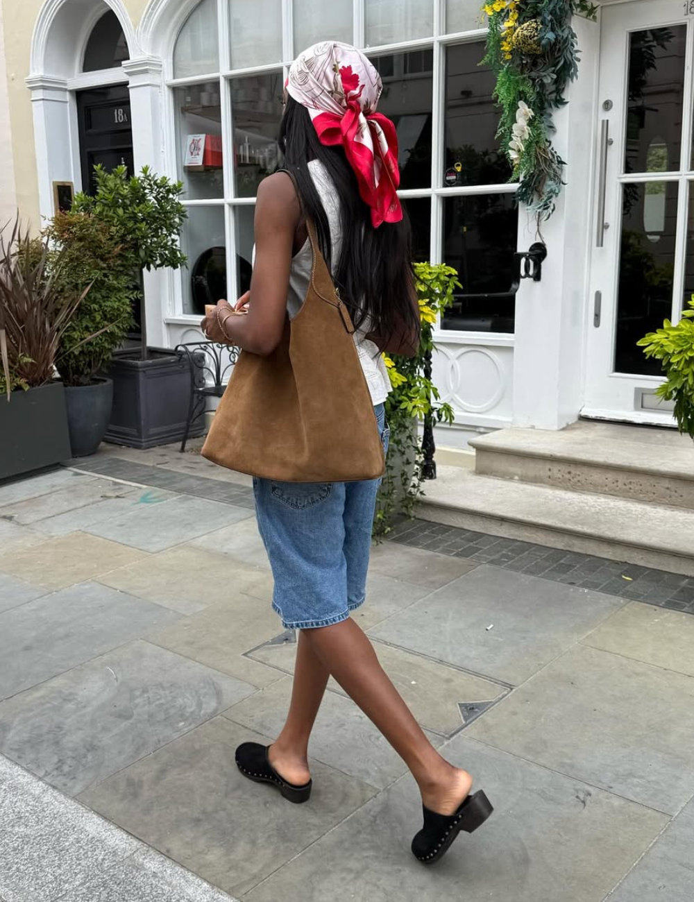Nesta cena, a modelo exibe sapatos do verão 2026, destacando um design contemporâneo com um salto robusto e detalhes em couro. A combinação com shorts jeans e uma blusa leve cria um visual fresco e descontraído, ideal para a temporada.