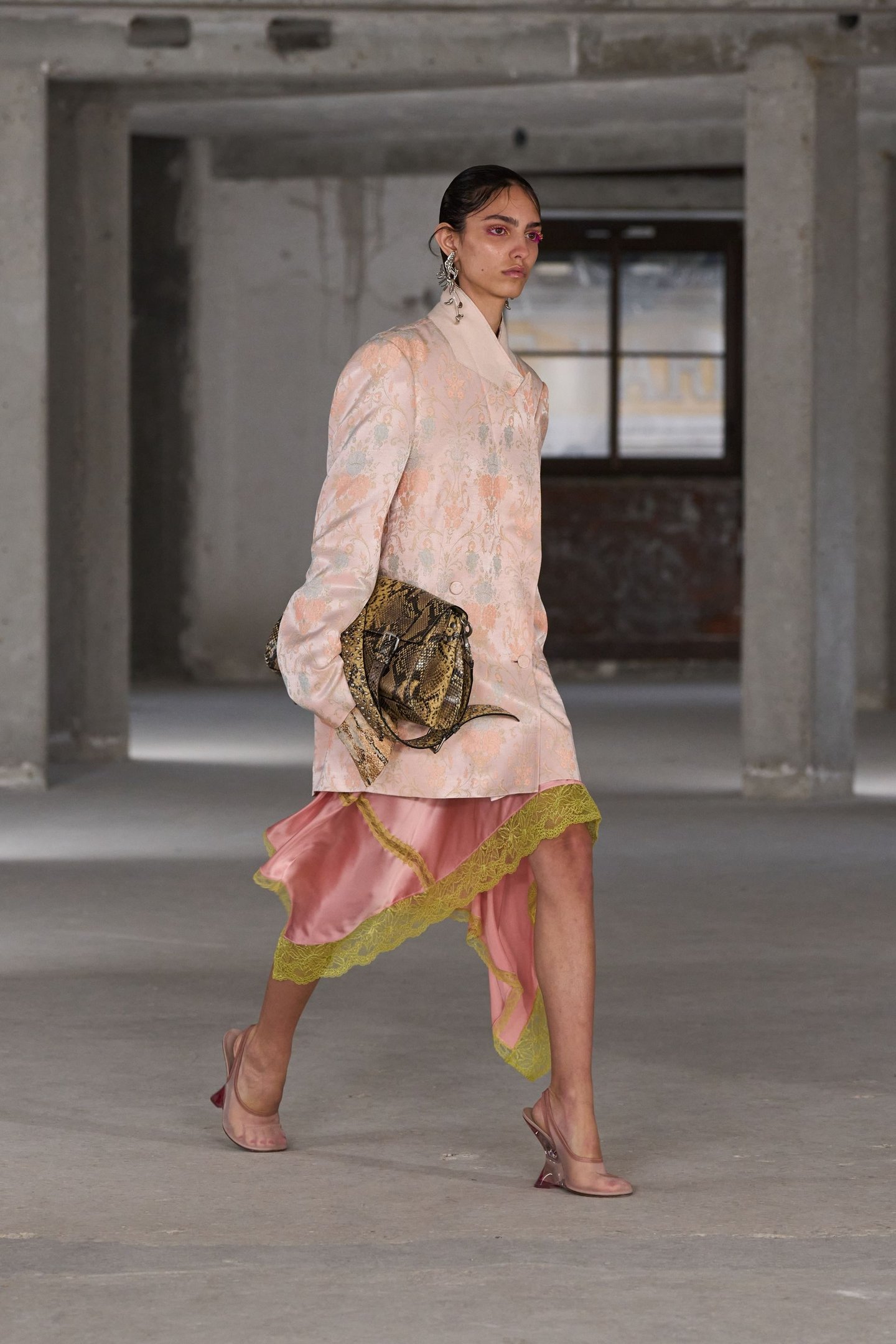 Modelo com blazer estampado e slip dress assimétrico em tons de rosa e verde. Bolsa de cobra e salto transparente.