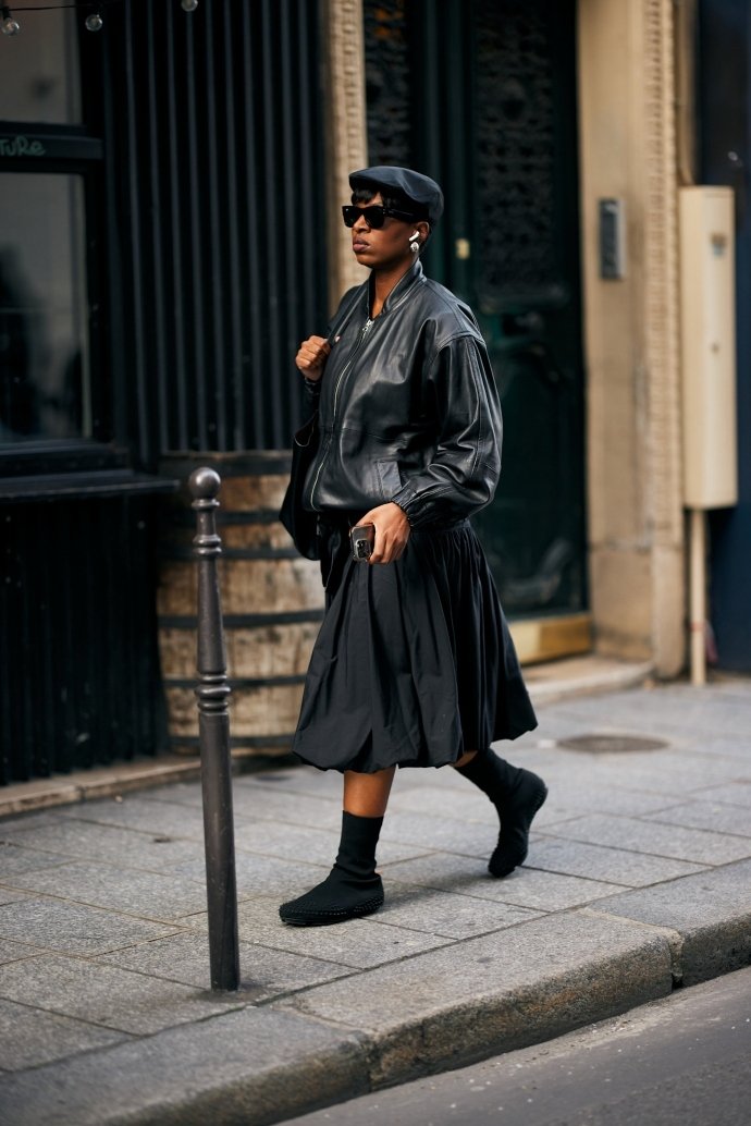 Pessoa com jaqueta de couro e saia preta andando pela rua, estilo street style da PFW.