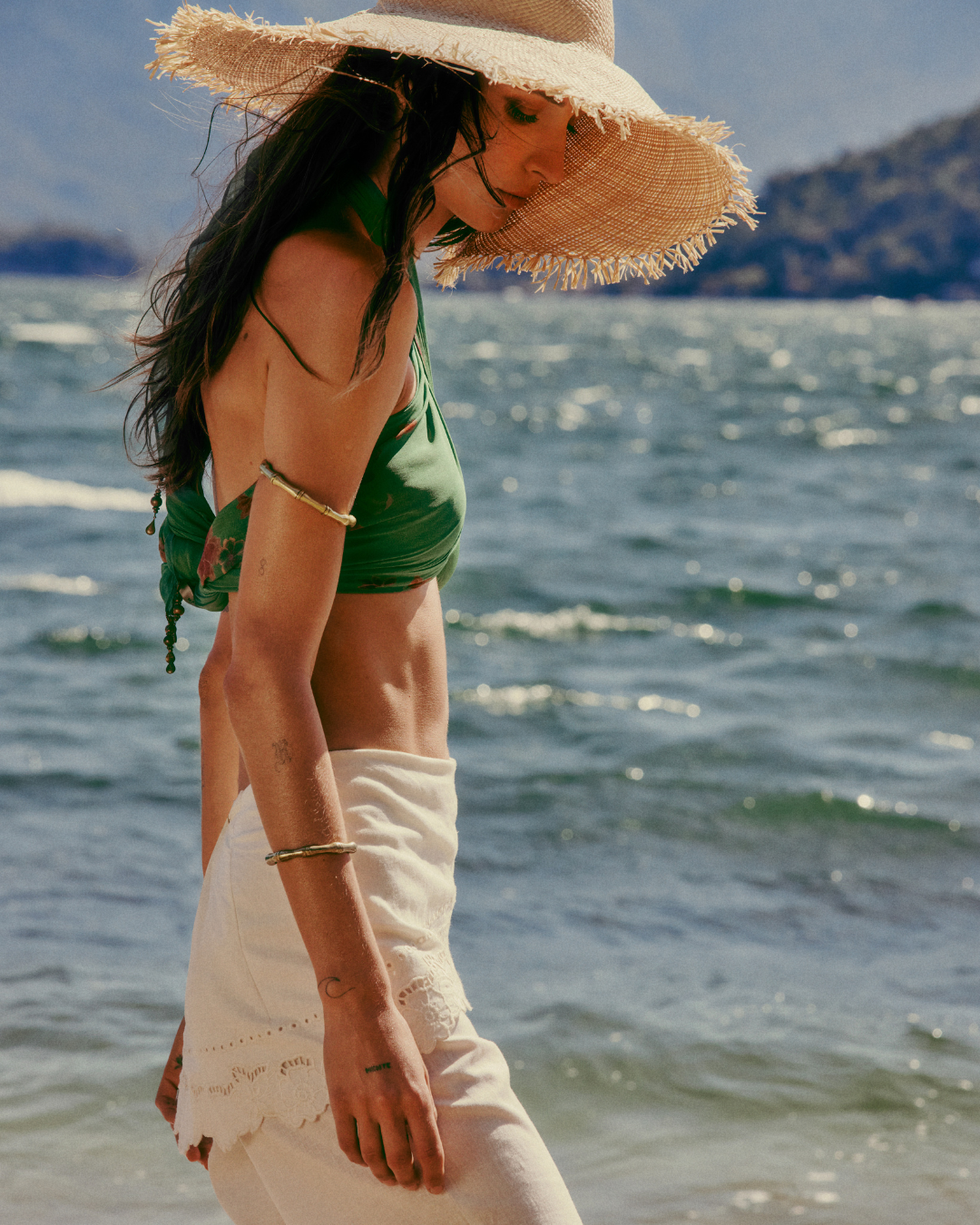 Mulher na praia com chapéu de palha e top verde, destacando tendências de alto verão.