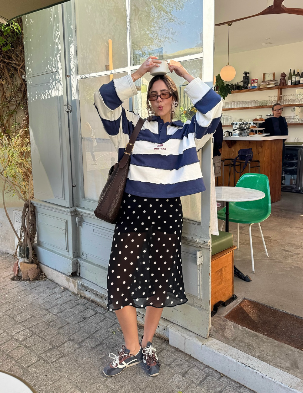 Mulher com saia de poás e tênis, em frente a café. Os tênis sugerem conforto e estilo casual.