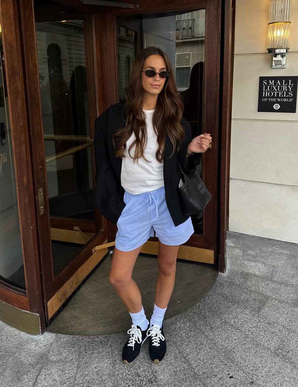 Mulher com roupa casual em frente a hotel, usando shorts azul claro e tênis confortável feminino preto.