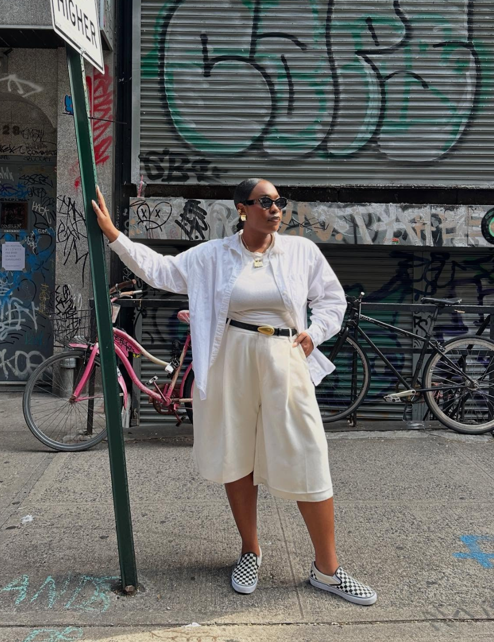 Pessoa usando óculos escuros, roupa branca e tênis confortável feminino xadrez em uma rua com grafites e bicicletas.