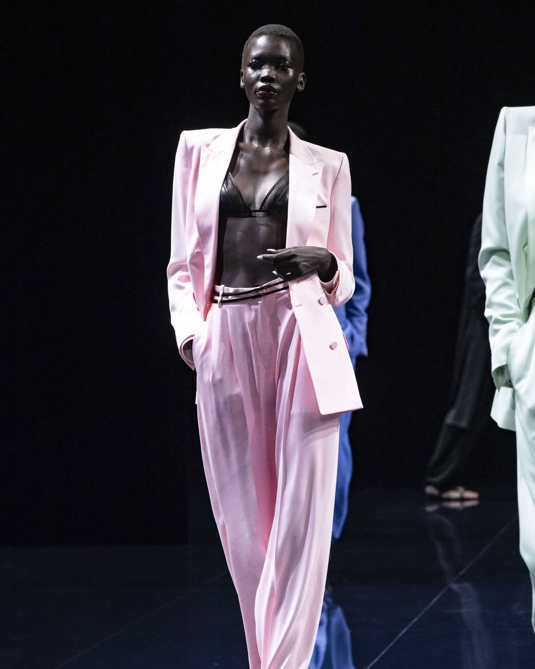 Elegante modelo em passarela, vestindo terno rosa bebê com blusa preta. Looks marcantes e sofisticados no desfile.