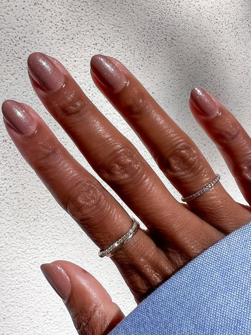 Ideias de unhas nude com acabamento brilhante e anéis prateados minimalistas, destacando a elegância sutil.