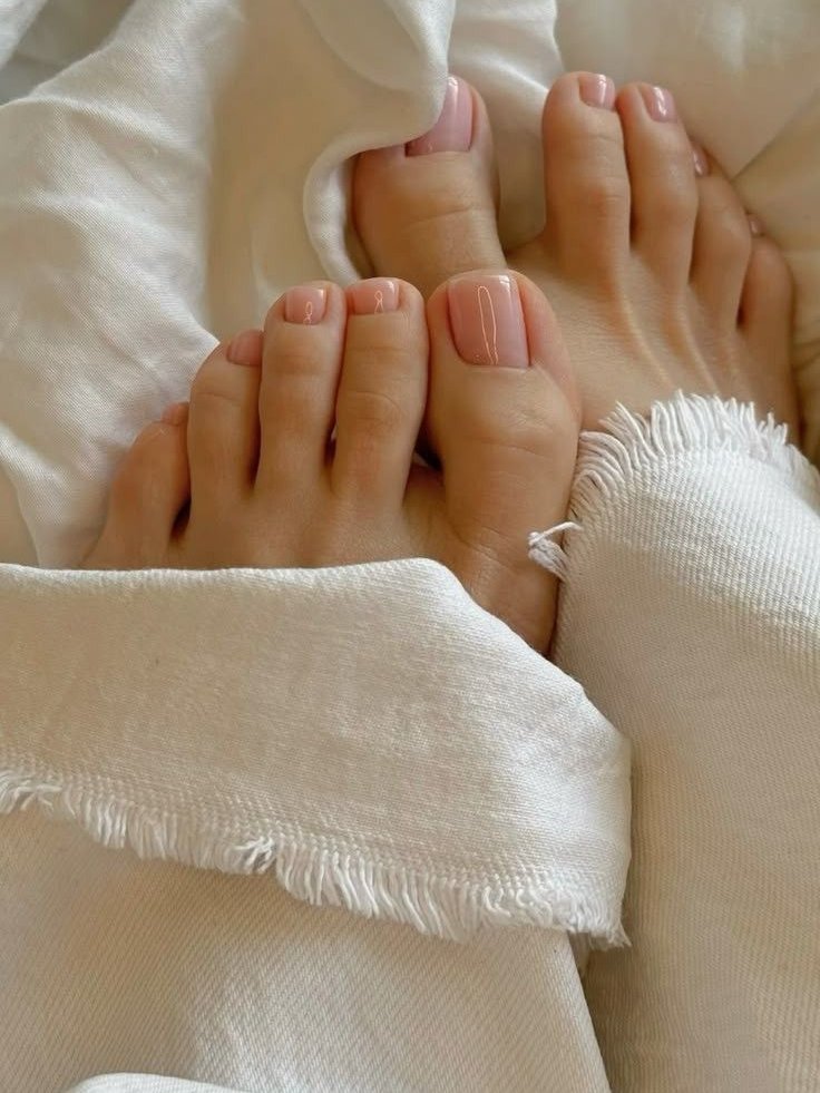 Ideias de unhas dos pés com esmalte nude, destacando simplicidade e elegância sobre tecido branco.