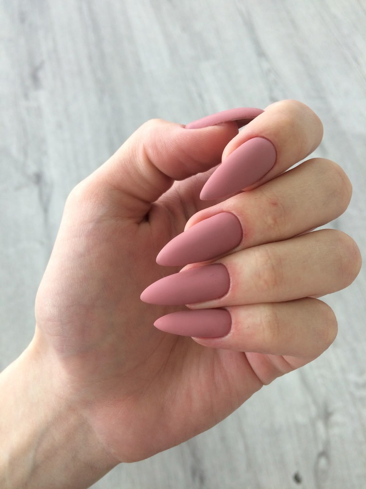 Unhas básicas em formato stiletto, com acabamento fosco na cor rosa nude, destacam-se pela elegância e sofisticação. O tom neutro é ideal para diversas ocasiões, equilibrando o visual. Esse estilo é uma tendência atual na moda e beleza, proporcionando um