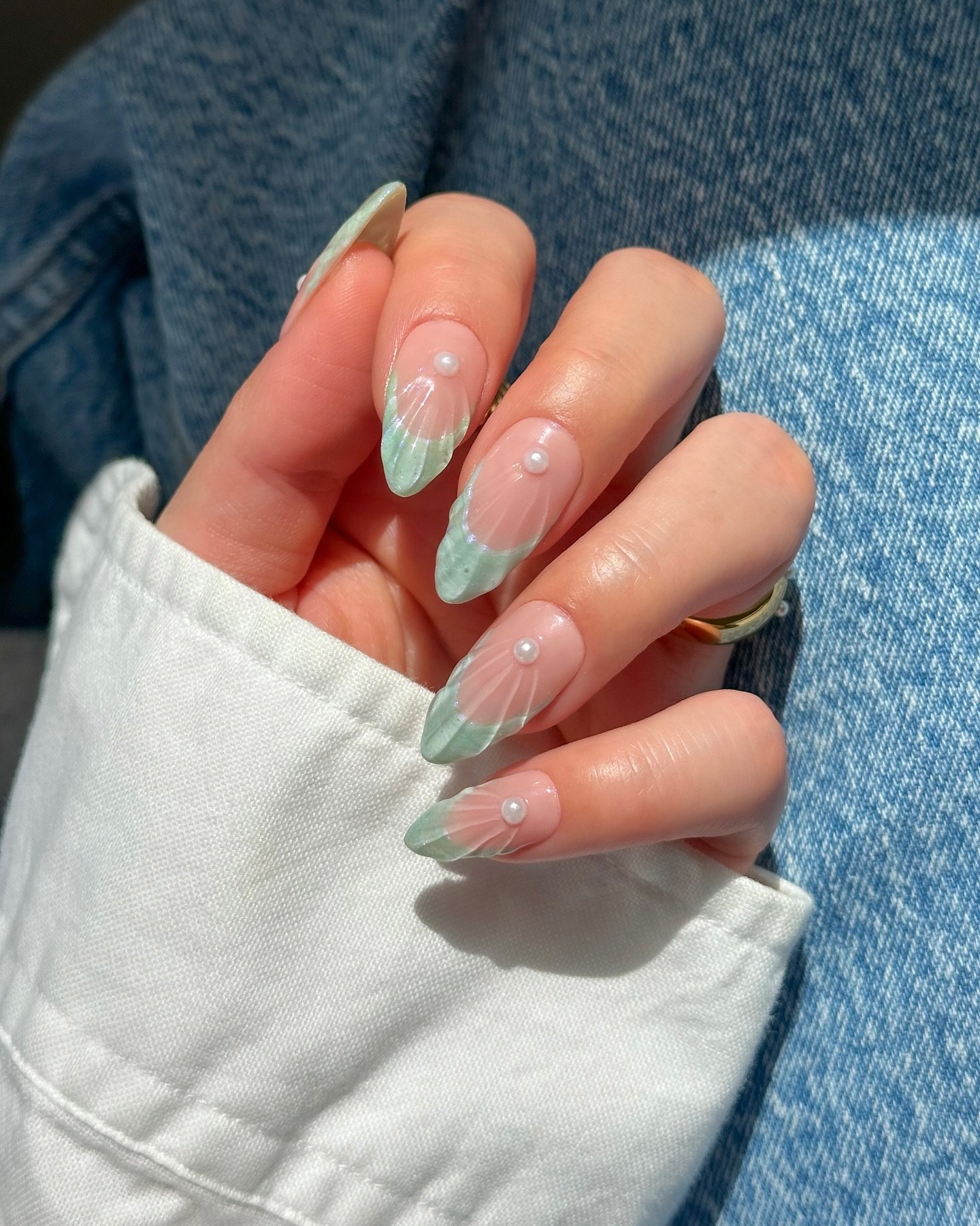 Unhas claras e delicadas pintadas com francesinha azul e aplicações de pérolas.