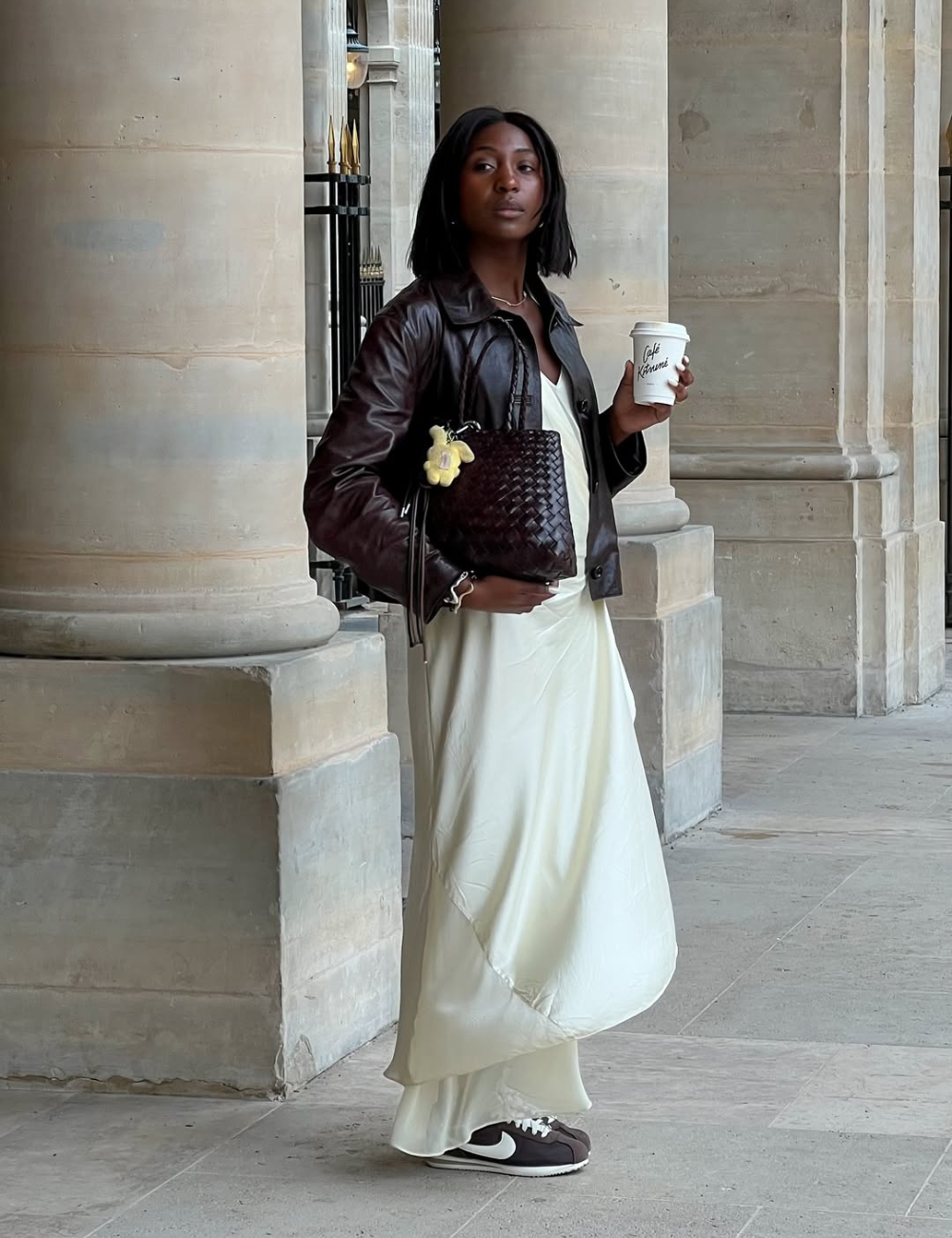 O vestido acetinado, em tom claro, destaca-se pela fluidez e elegância, ideal para diversas ocasiões. Combinado com uma jaqueta de couro escura, a produção ganha um toque moderno e despojado. A escolha de tênis traz conforto e um ar casual.