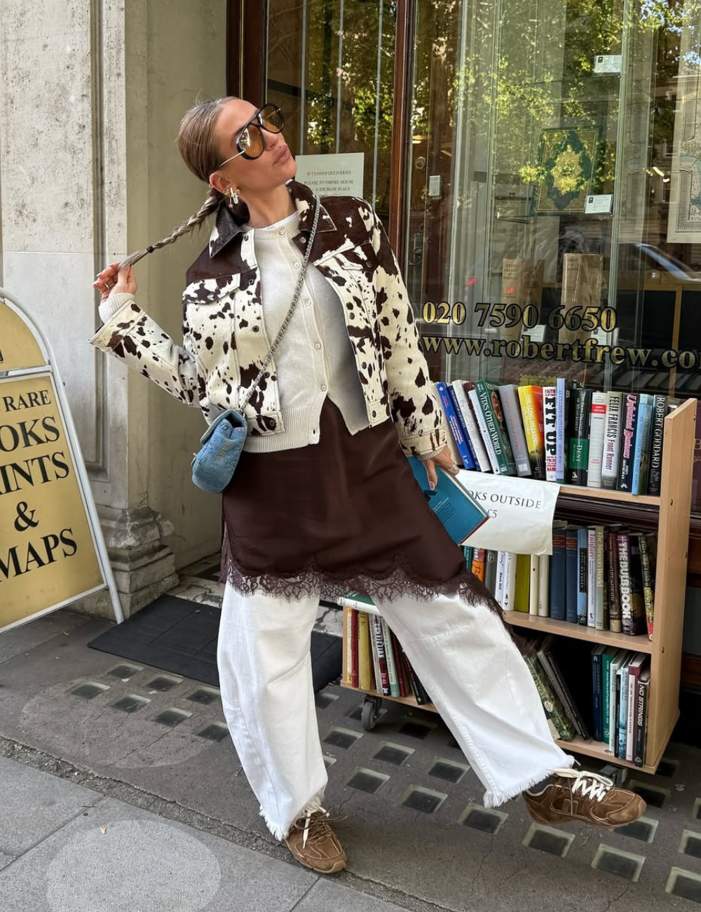 A imagem apresenta uma jovem estilosa usando um vestido acetinado marrom, que se destaca pela textura suave e brilho sutil. O vestido é combinado com uma jaqueta estampada em preto e branco, criando um contraste interessante. 