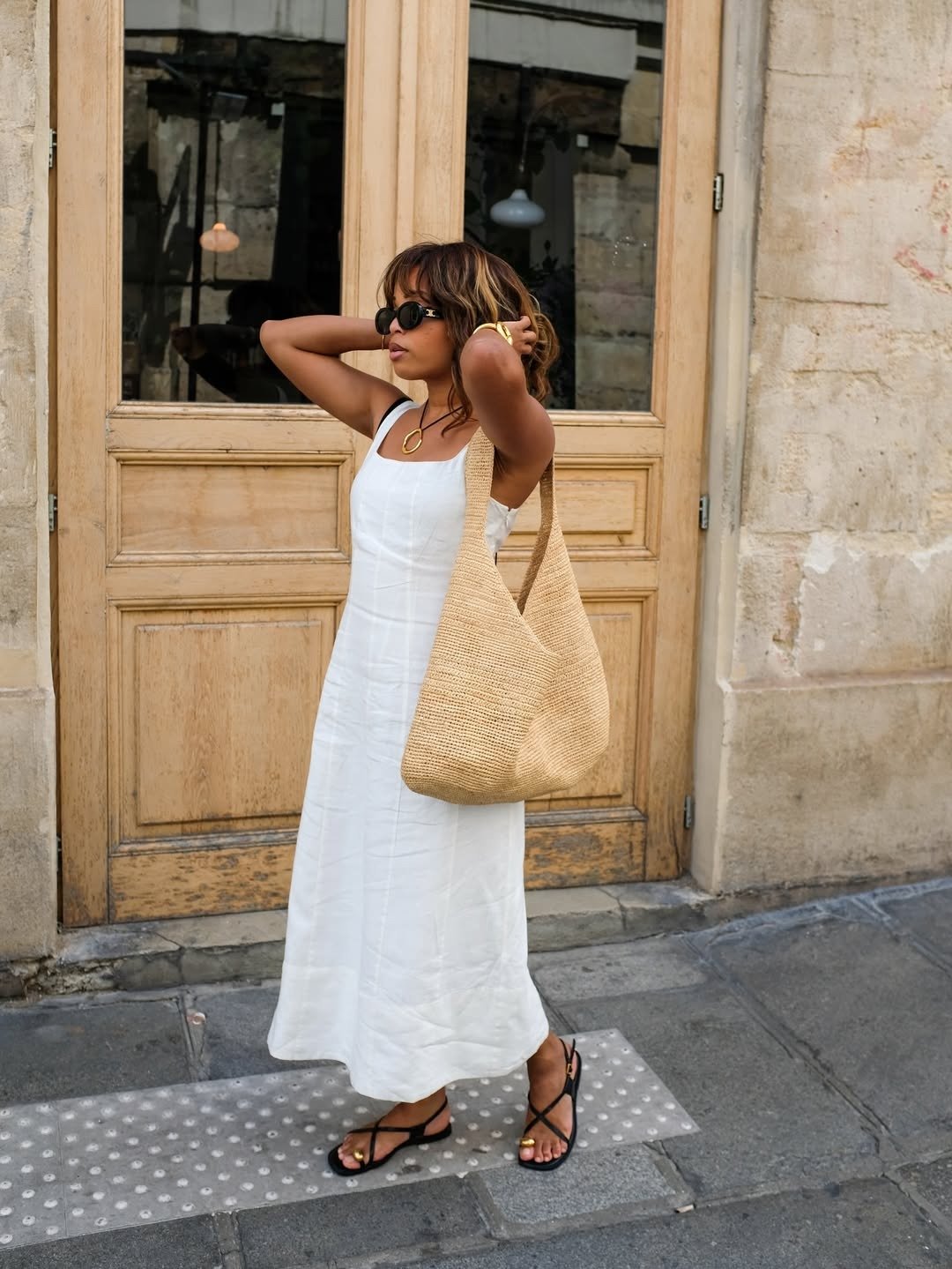 Vestidos midi para o verão são uma escolha ideal para quem busca conforto e estilo. A imagem mostra uma mulher usando um vestido midi branco, com alças finas, que destaca a leveza do tecido. Ela complementa o look com sandálias pretas e uma bolsa de palha