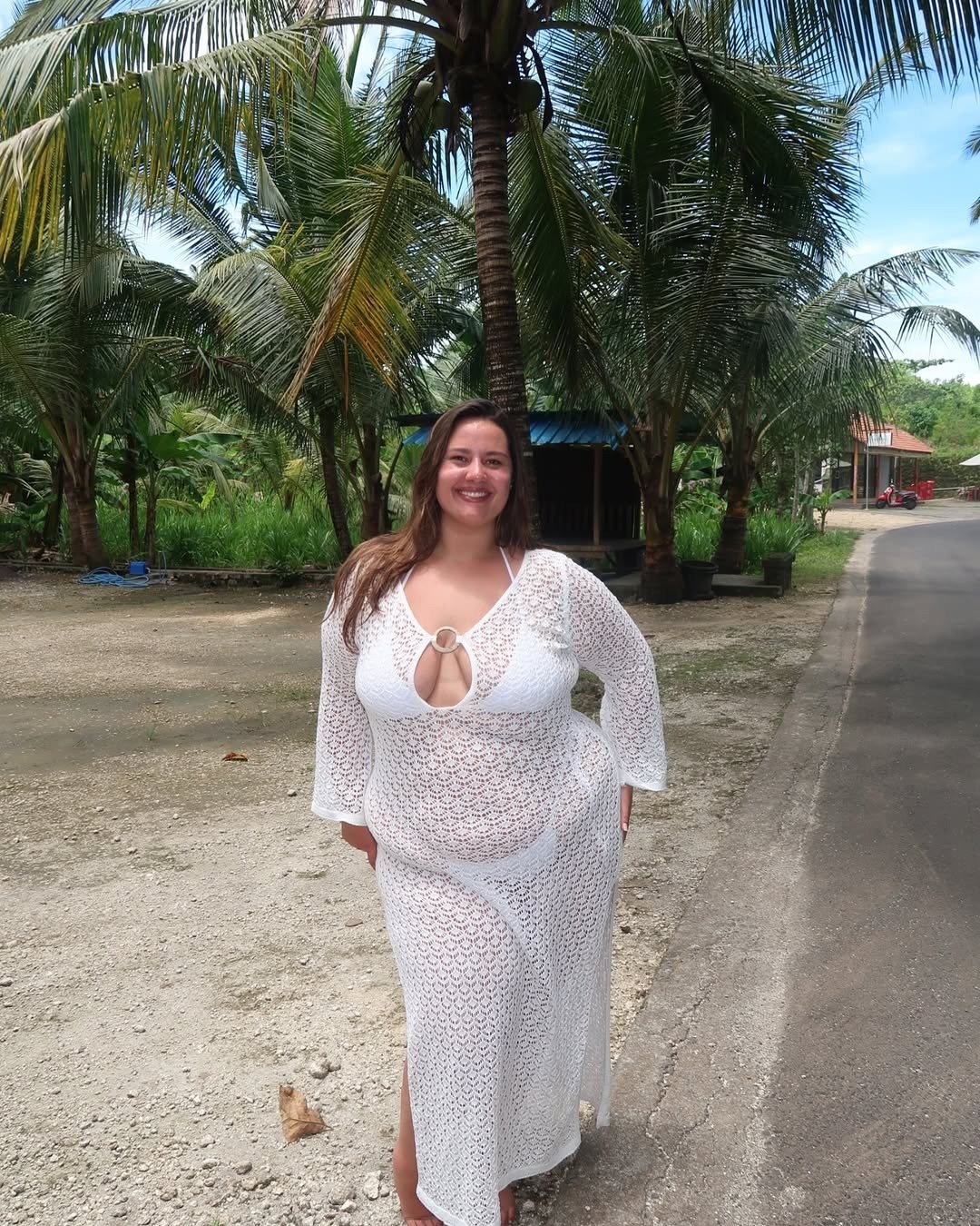 O vestido saída de praia é uma peça leve e arejada, ideal para os dias quentes. Nesta imagem, destaca-se um modelo branco, com detalhes em crochê e um decote em formato de gota, que confere um toque elegante. As mangas longas e a fenda lateral proporciona
