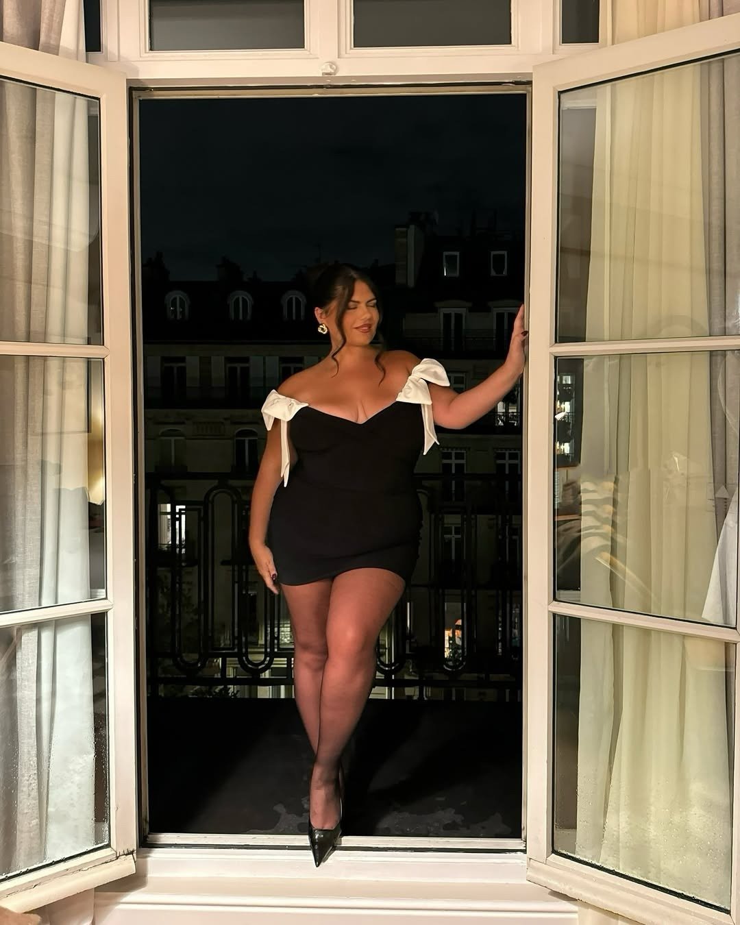 A imagem apresenta uma mulher em um vestidos de formatura preto, com detalhes em branco nas mangas. O modelo é justo e destaca a silhueta, ideal para ocasiões festivas.