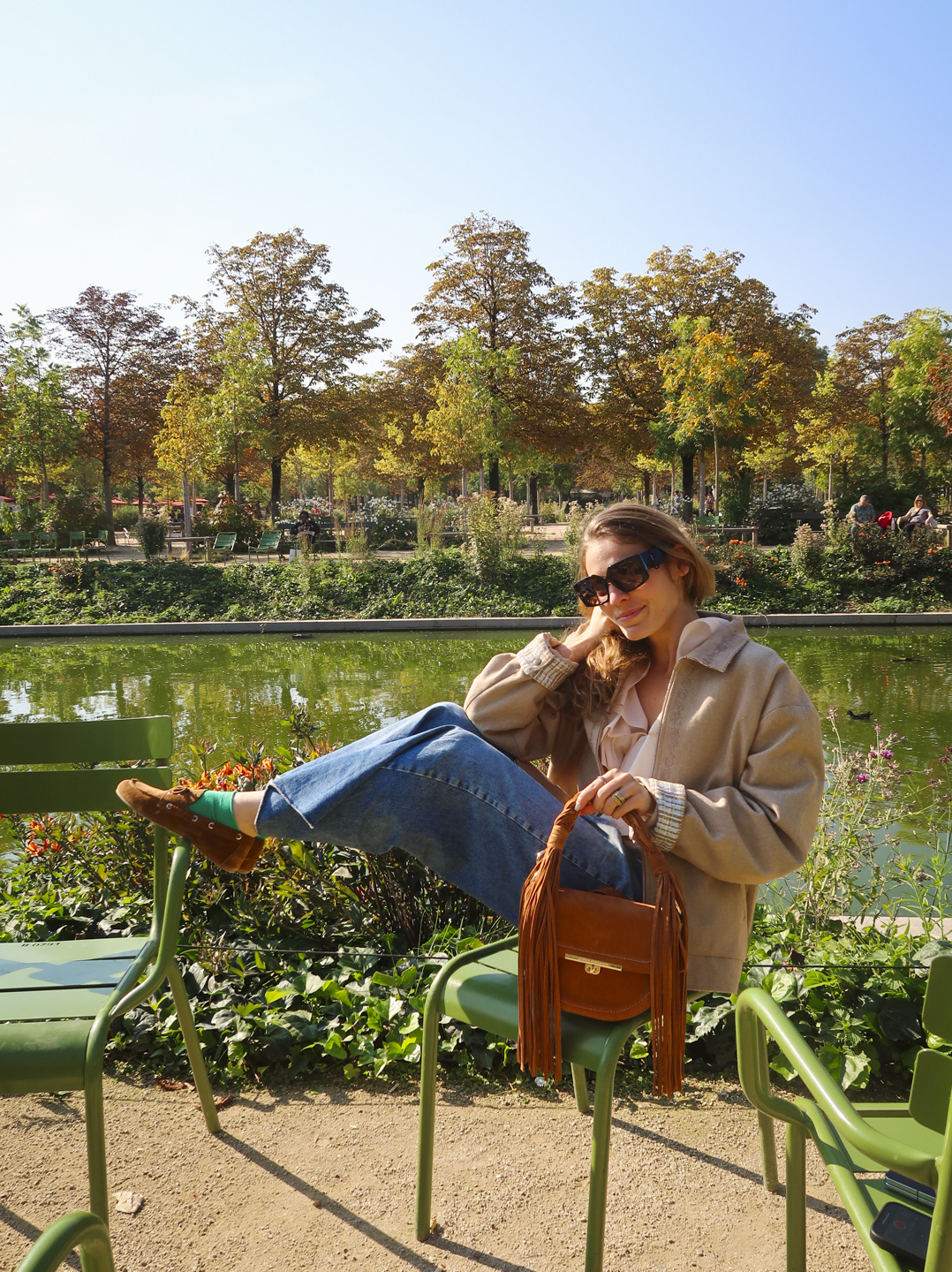 Pessoa sentada em cadeira ao ar livre, sorrindo, usando jeans e uma jaqueta. sapato confortável para viajar. Fundo de parque.