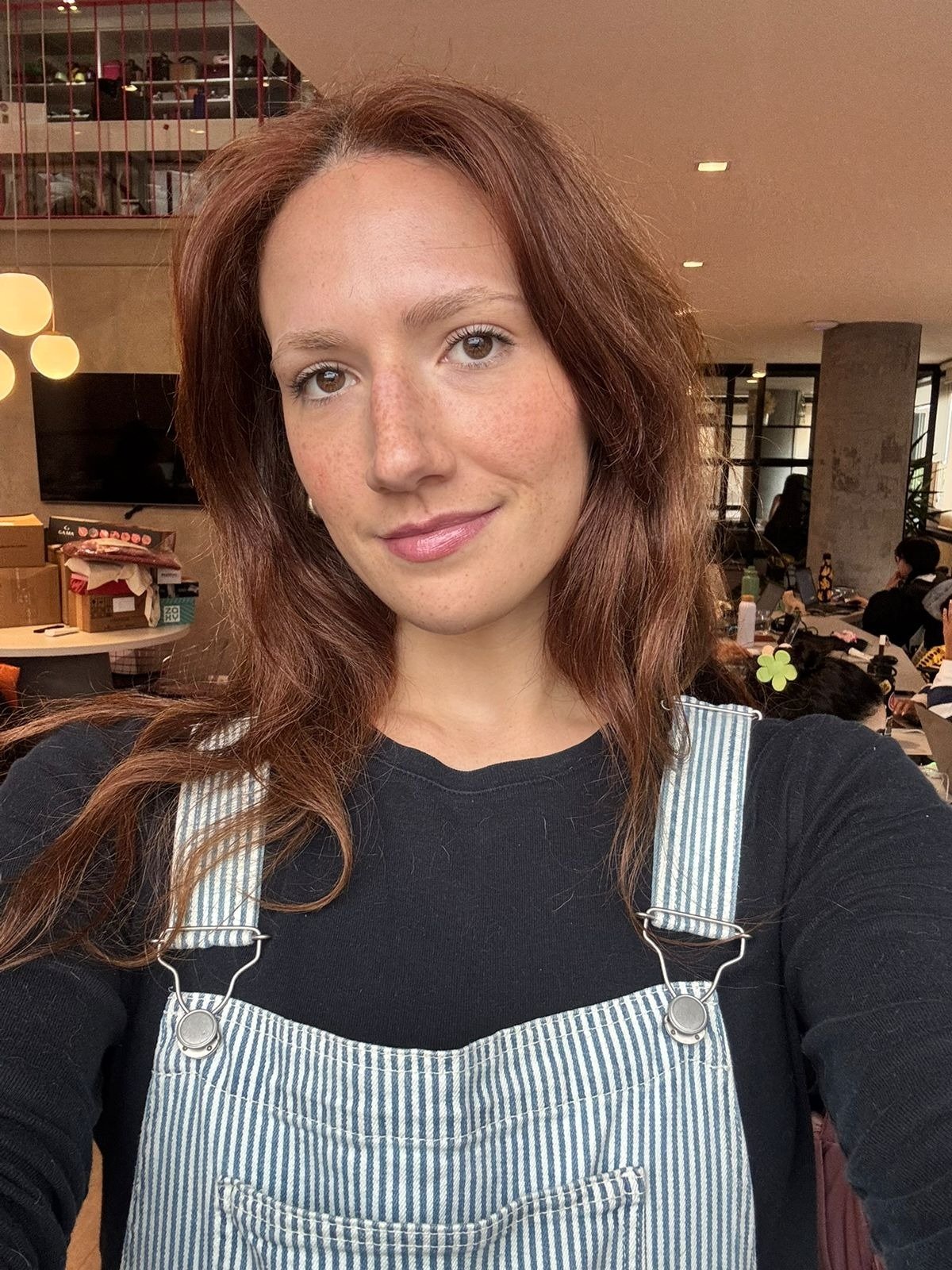 A imagem apresenta uma mulher com cabelo castanho avermelhado, usando um macacão listrado e uma blusa preta. Seus lábios estão destacados por um Lip Oil Epidrat Hyalu, um lip oil hidratante e com proteção solar