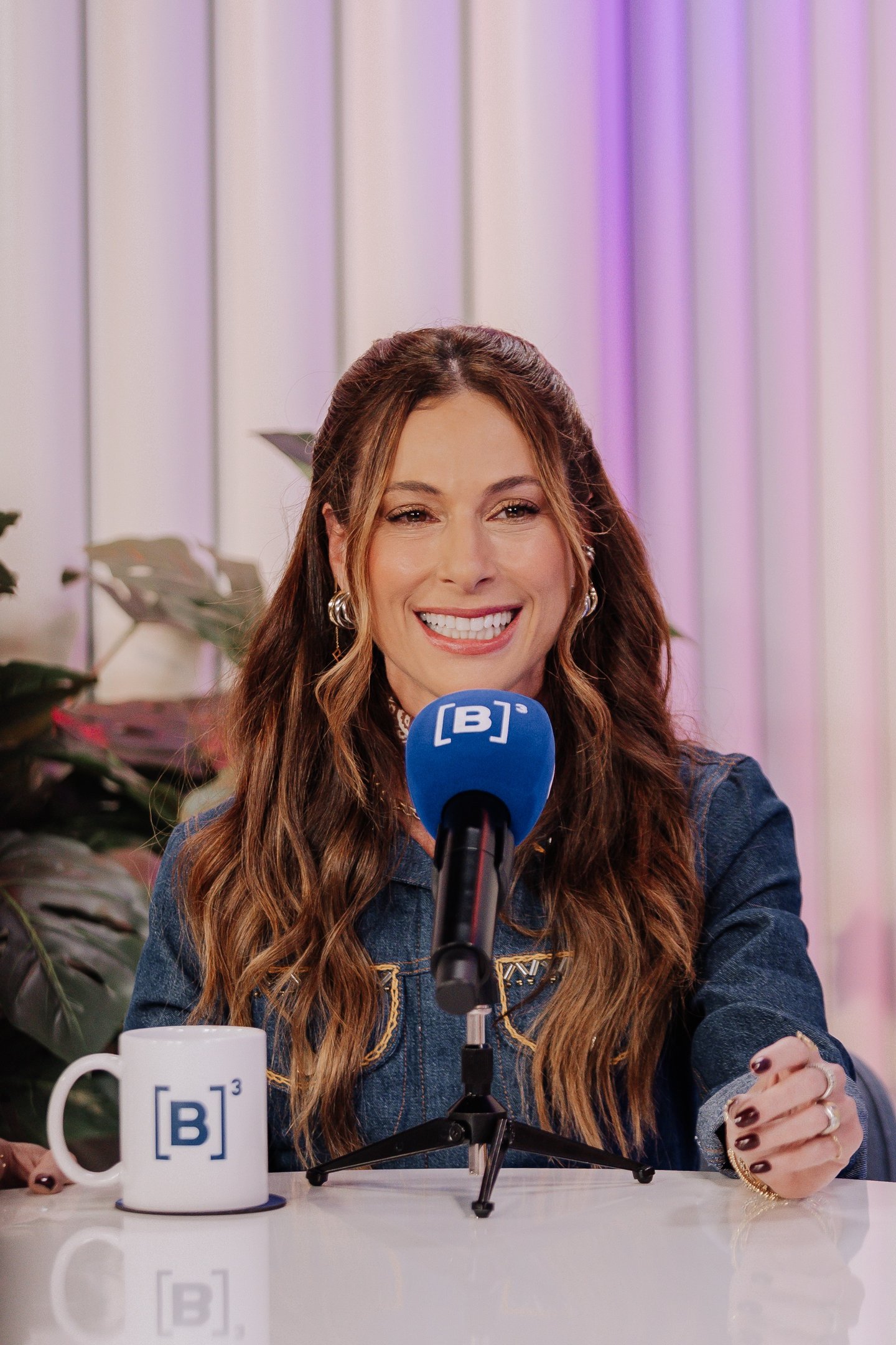 Anny Meisler sorri com elegância em jaqueta jeans de modelagem ajustada, transmitindo leveza e simpatia em ambiente moderno.