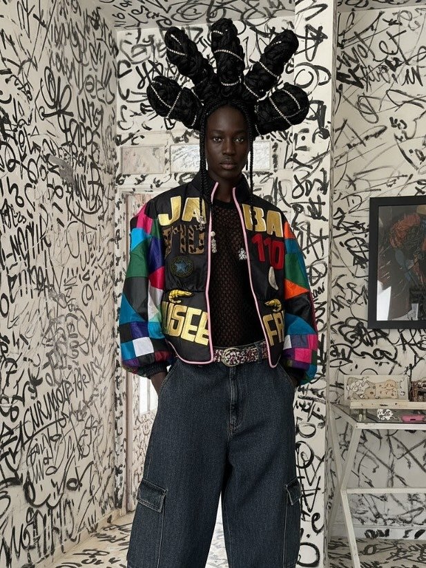 Modelo posa com jaqueta colorida oversized em patchwork vibrante, blusa de tela preta e calça cargo jeans. Afrofuturismo