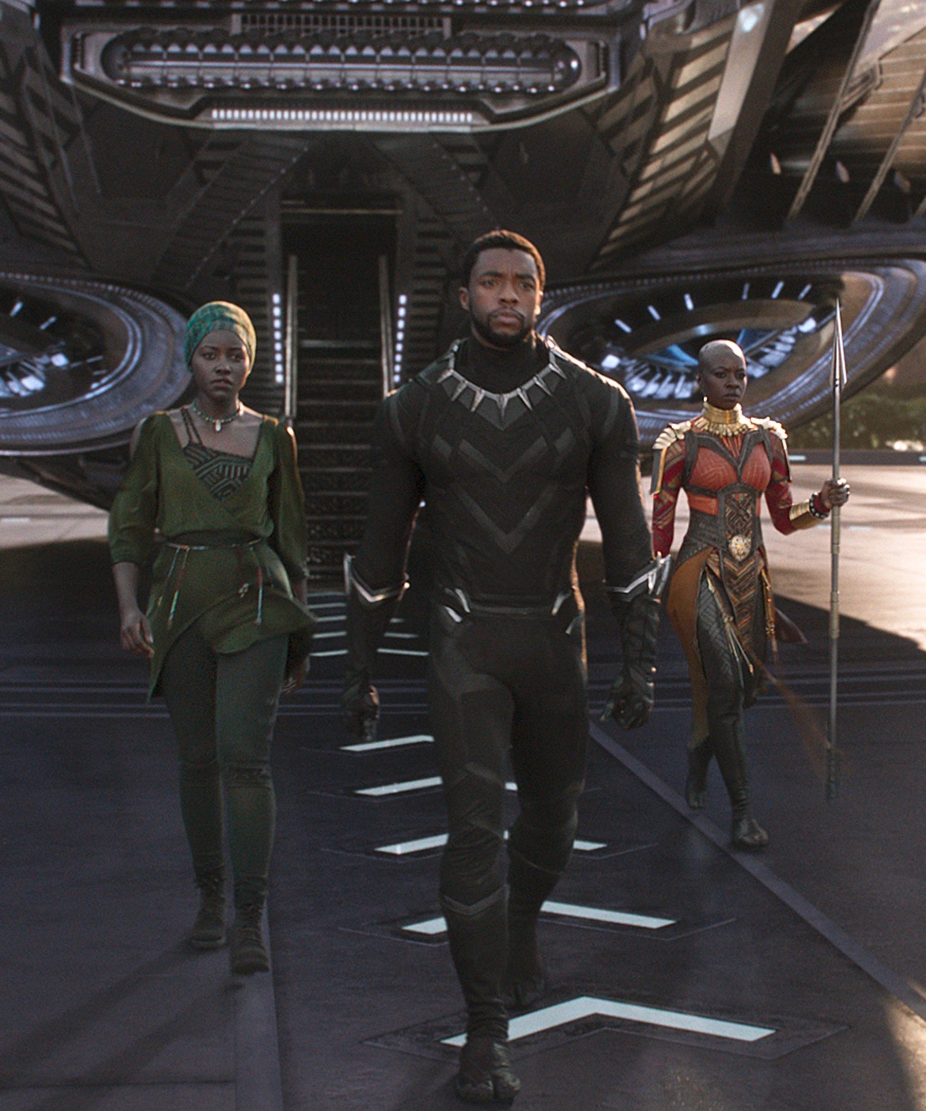 Trio caminha com postura firme em cenário futurista, vestindo peças afrofuturistas com modelagens estruturadas em preto,