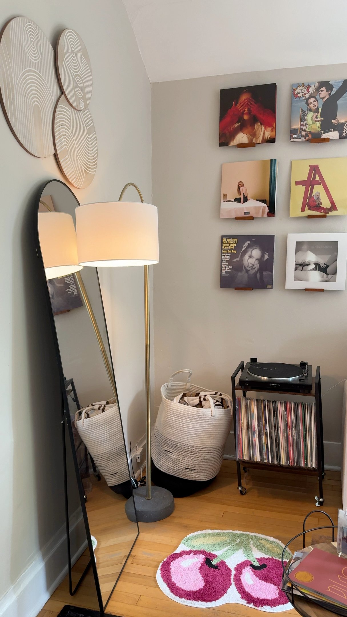Quarto de adolescente com decoração minimalista em tons neutros, tapete colorido de cerejas, estante de vinis e iluminação