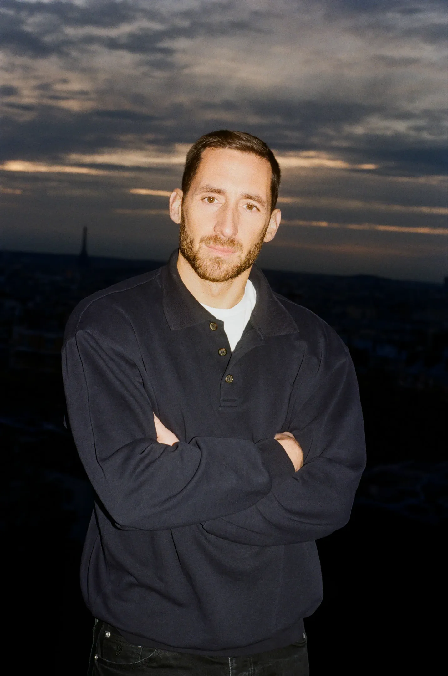 Antonin Tron exibe um estilo casual e contemporâneo, usando uma polo escura que reflete a estética minimalista.