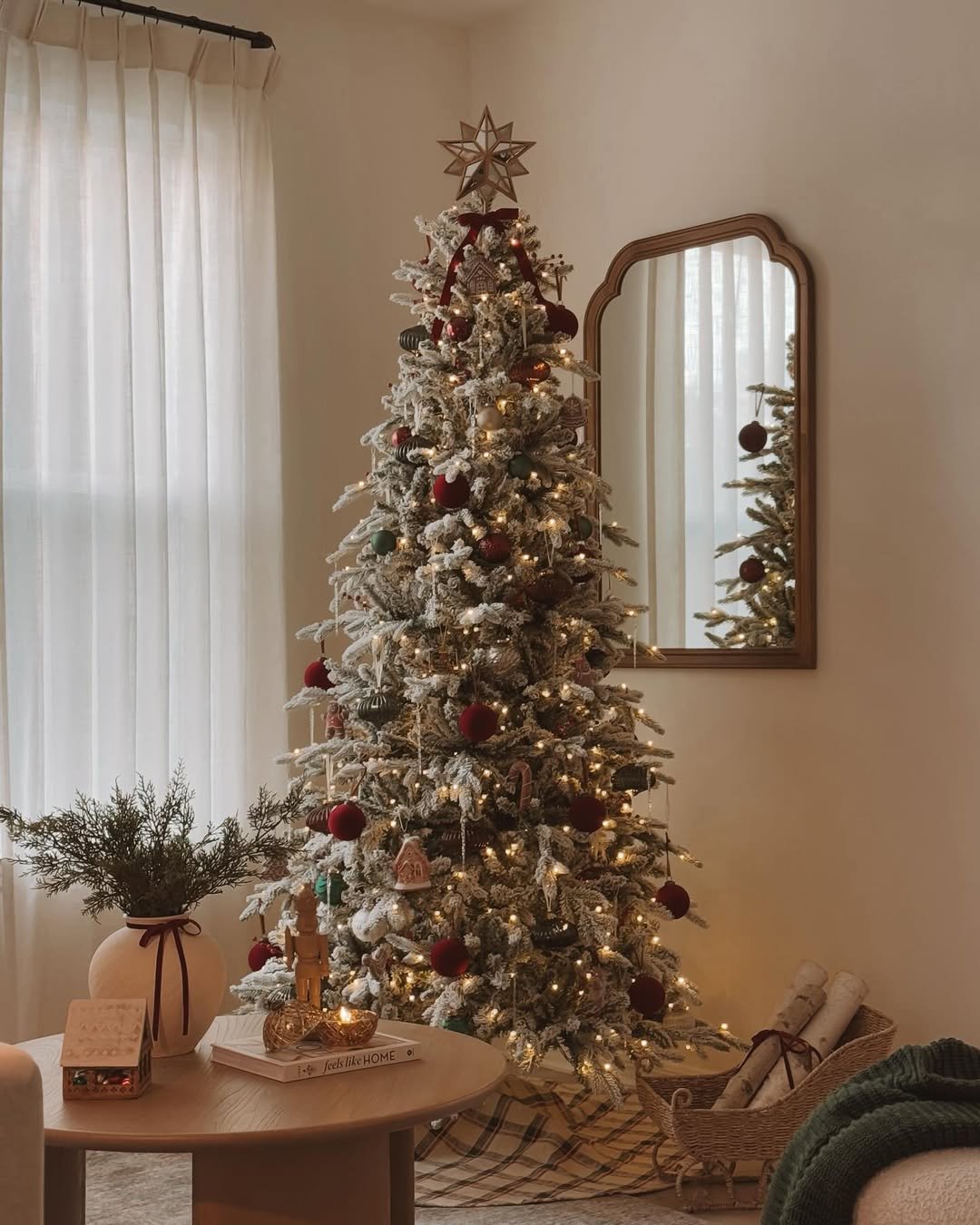 Árvore de Natal com efeito neve, enfeites em vermelho, verde e dourado, luzes quentes e estrela dourada no topo.