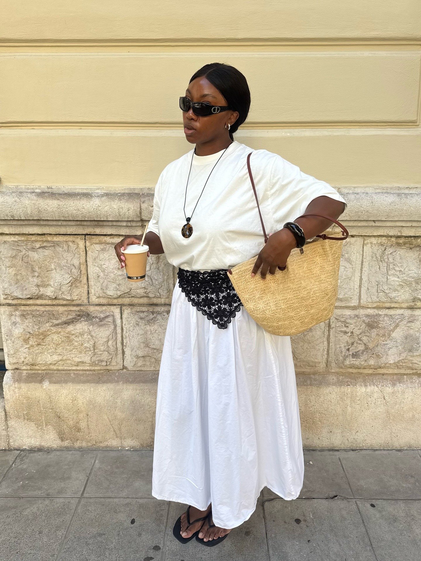 Mulher posa com looks com bandana preta de renda sobre vestido branco longo, camiseta solta, bolsa de palha e acessórios