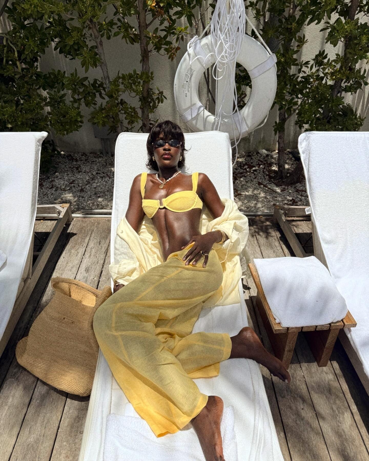A imagem apresenta uma mulher elegante relaxando em espreguiçadeiras, vestindo um biquíni amarelo vibrante, que é uma das