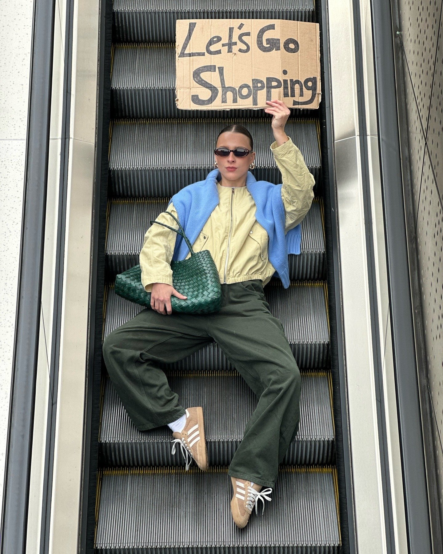 Uma jovem estilosa está sentada em uma escada rolante, segurando um cartaz que diz