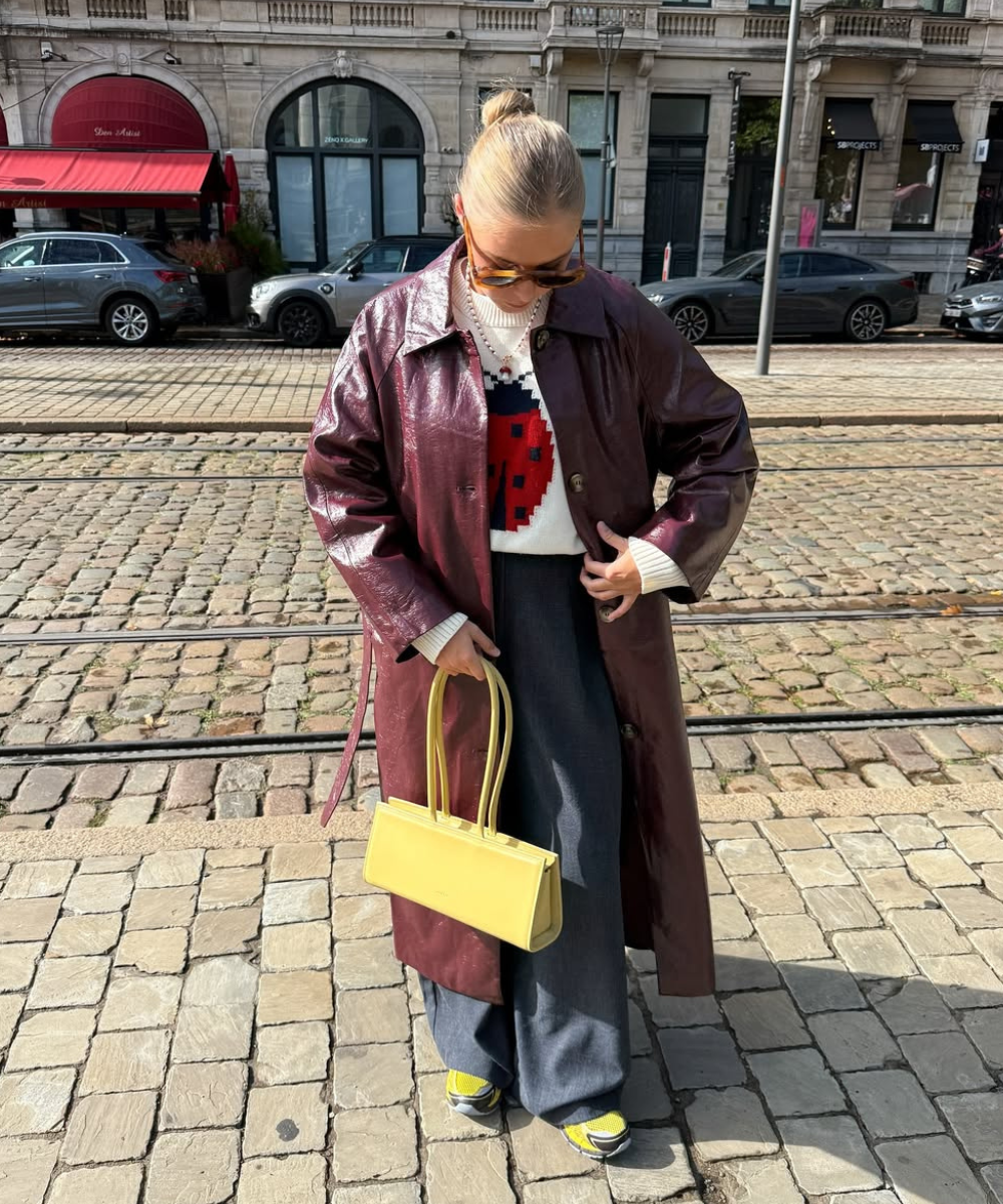 Look moderno com bolsa de ombro estilosa amarela, casaco brilhante e calças largas, ideal para um dia urbano.