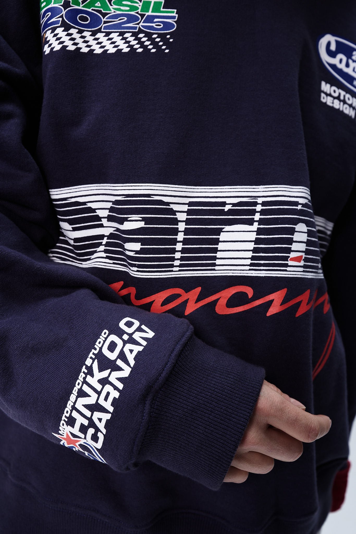A imagem apresenta uma peça de vestuário, um moletom na cor azul-marinho, que destaca elementos de design relacionados a corridas. O logo 