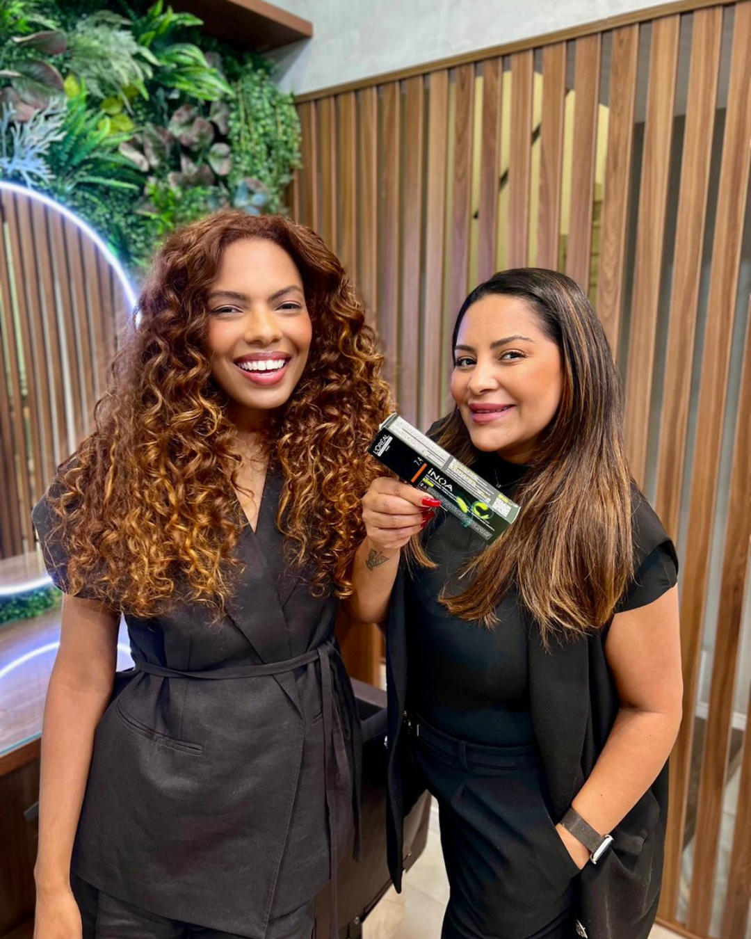 Modelo sorridente segura produto L\'Oréal Inoa para coloração de cabelos crespos e cacheados, com profissional da marca. 