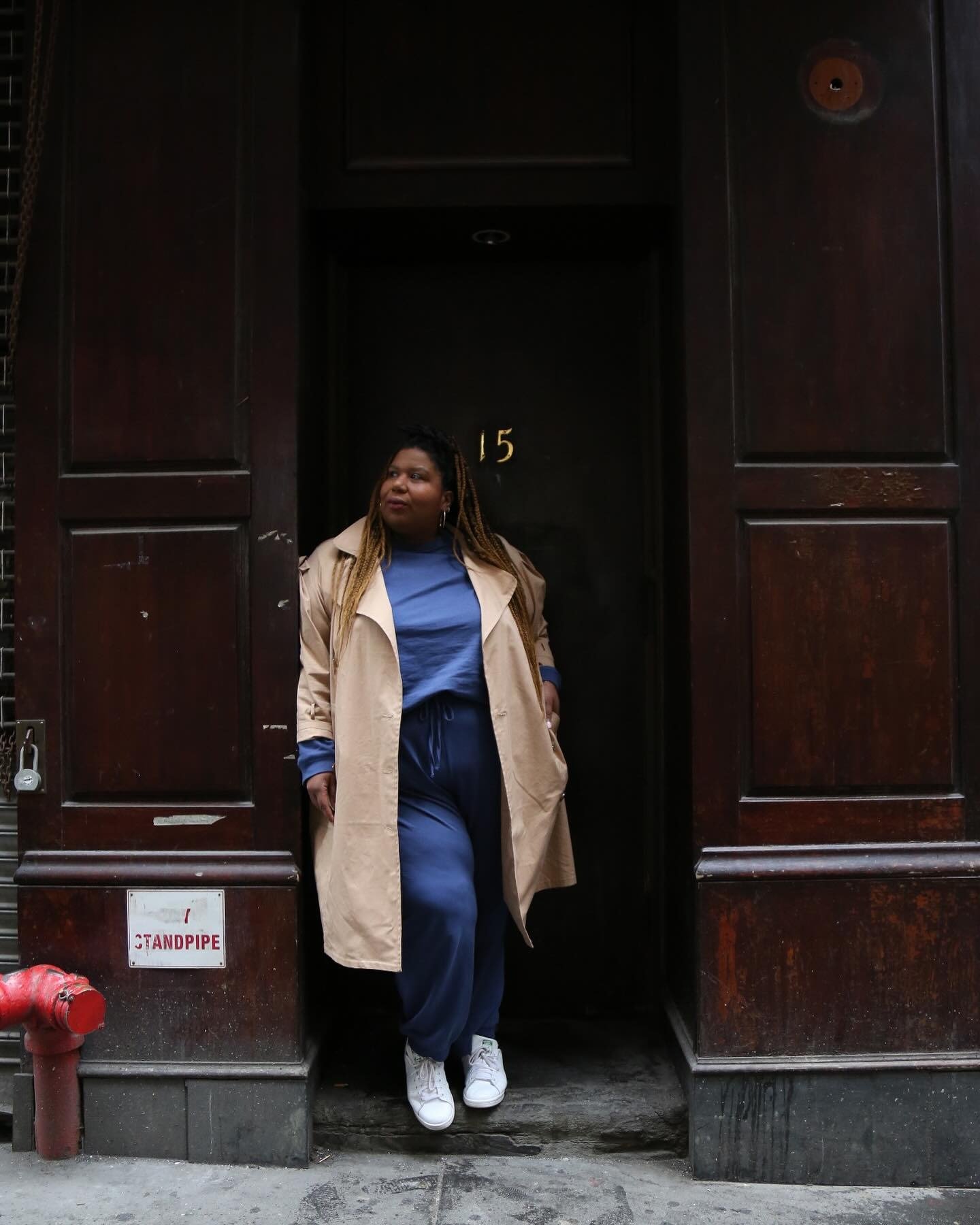 Modelo posa encostada em porta escura com calça jeans azul de modelagem ampla e tênis branco, combinando conforto e estilo