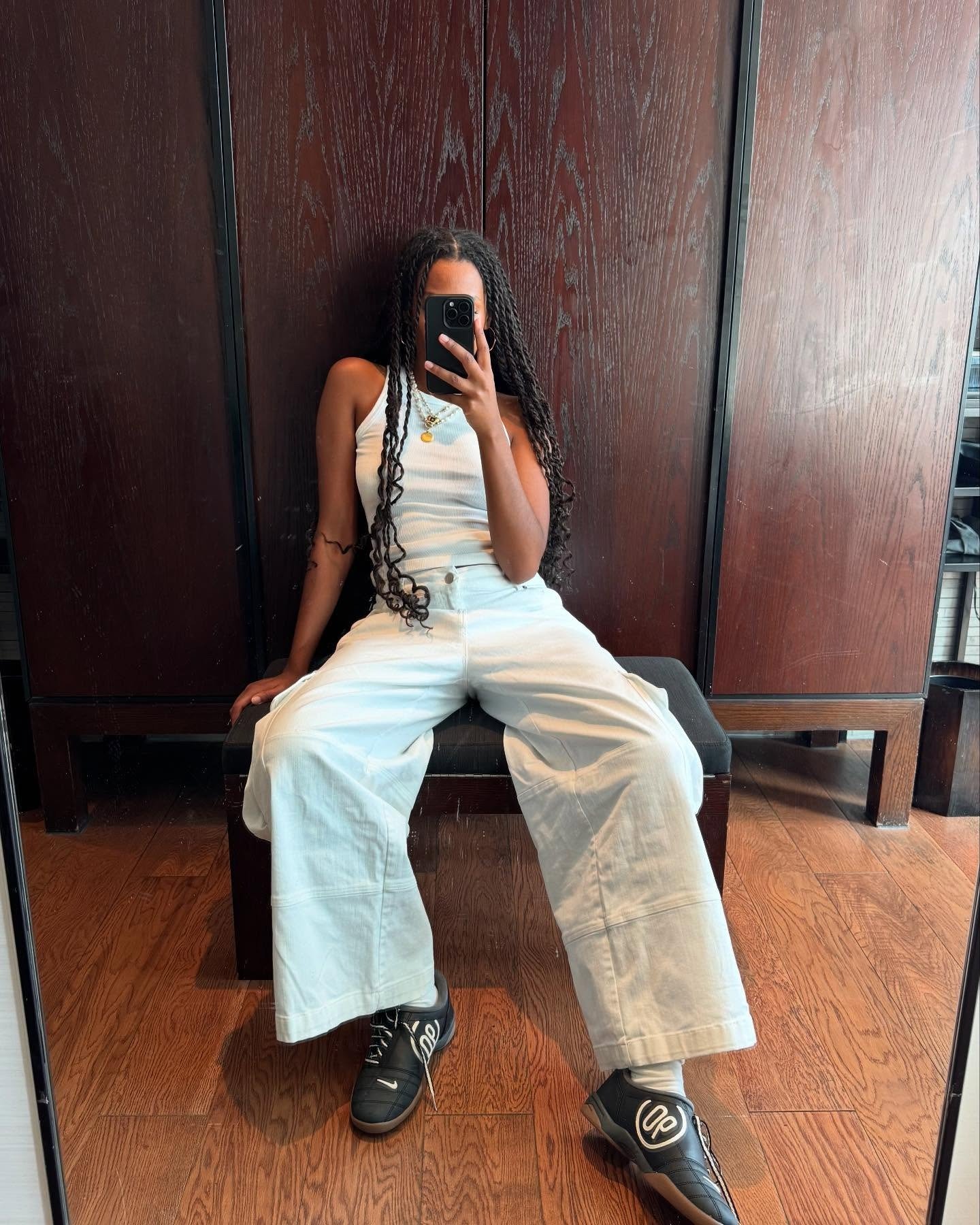 Modelo senta com postura descontraída usando calça jeans branca de modelagem ampla e tênis preto com detalhes brancos, em