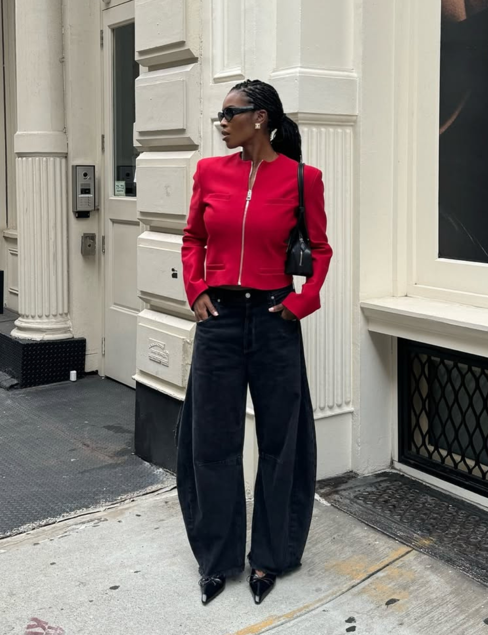 Uma das calças jeans tendência de 2026 destaca-se por modelos amplos e sofisticados, como os vistos na imagem. A combinação de uma jaqueta vermelha estruturada com calças jeans de lavagem escura cria um contraste marcante e moderno.