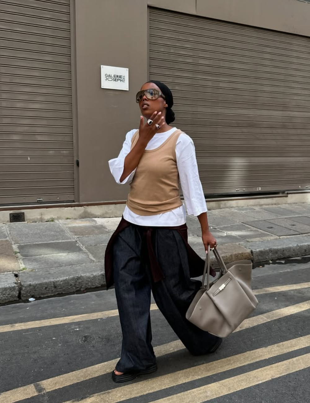 A imagem apresenta uma mulher estilosa usando calças jeans largas, uma tendência forte para 2026. Ela combina as calças com uma blusa branca de mangas longas e um colete bege.