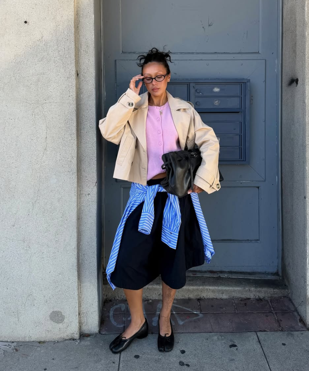 A combinação de uma camisa amarrada na cintura com uma jaqueta oversized e um top colorido traz um toque moderno e despojado. O uso de cores contrastantes, como o rosa e o azul listrado, destaca a criatividade no styling.