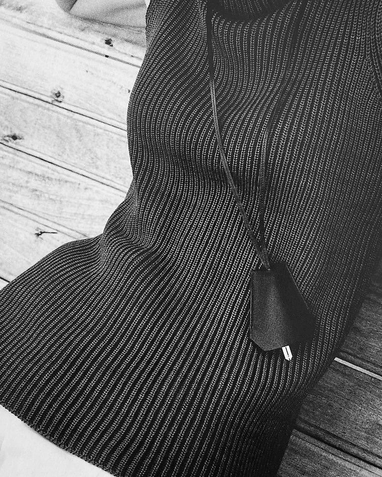 Colar funcional em couro preto com design minimalista complementa blusa de tricô texturizada, criando estilo moderno e