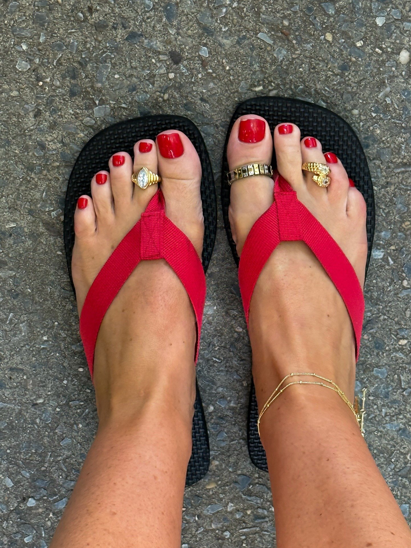 Os pés exibem esmalte vermelho vibrante, com anéis de dedo do pé em destaque: