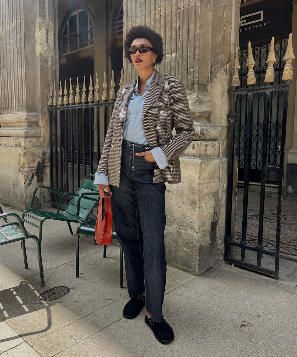 Modelo posa com postura confiante usando clog confortável preto, calça jeans reta, camisa azul clara e blazer xadrez, em