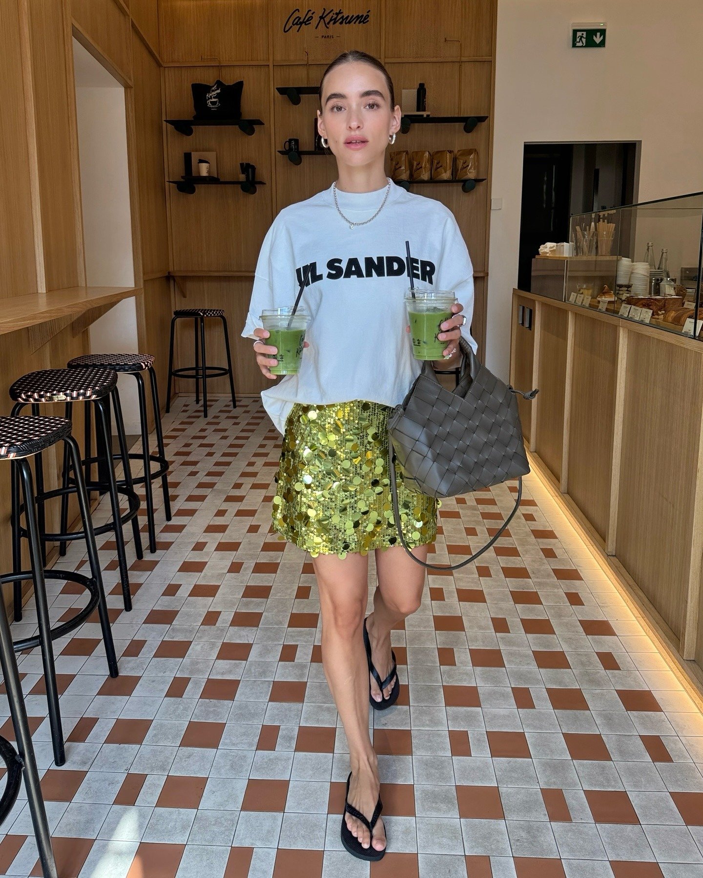 Modelo caminha segura em ambiente casual usando saia curta de paetê dourado, camiseta branca oversized e sandálias pretas,