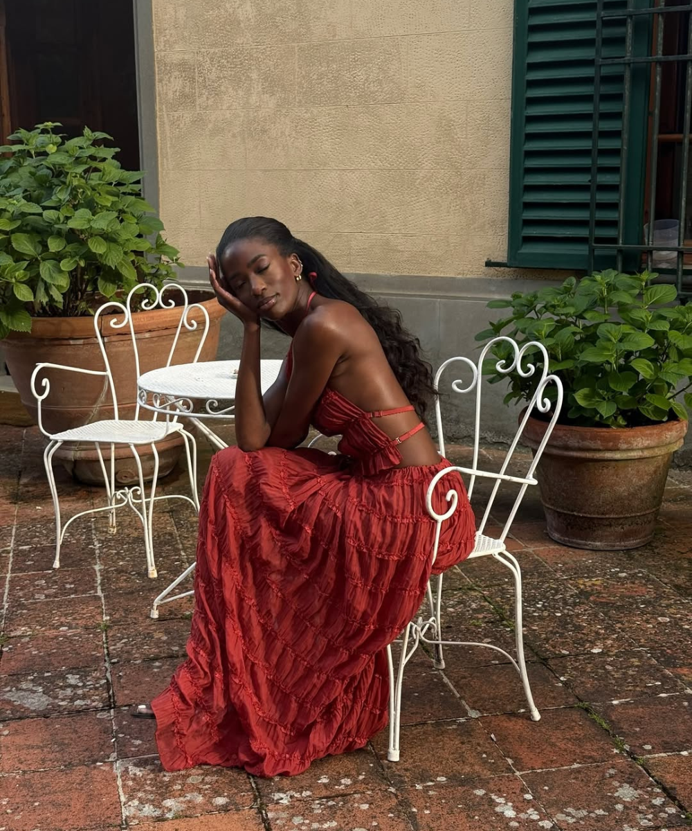 Modelo posa sentada com conjunto estiloso em tom terracota, top cropped com tiras e saia longa de tecido texturizado, em