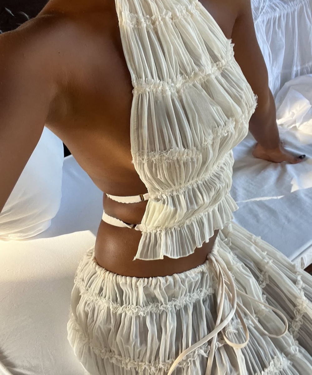 Conjunto estiloso em tecido leve off-white com babados franzidos, top assimétrico e saia fluida, criando visual delicado e