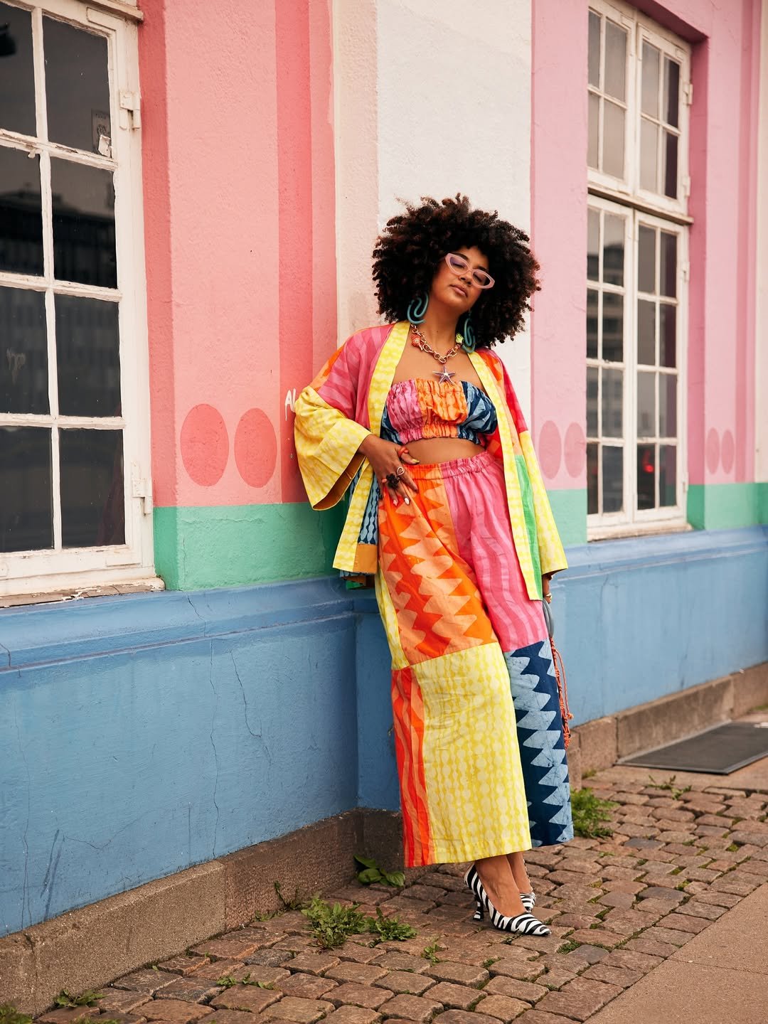 Mulher com look vibrante em tons de amarelo e azul, cores de Câncer para 2026, posa confiante em frente a parede colorida.