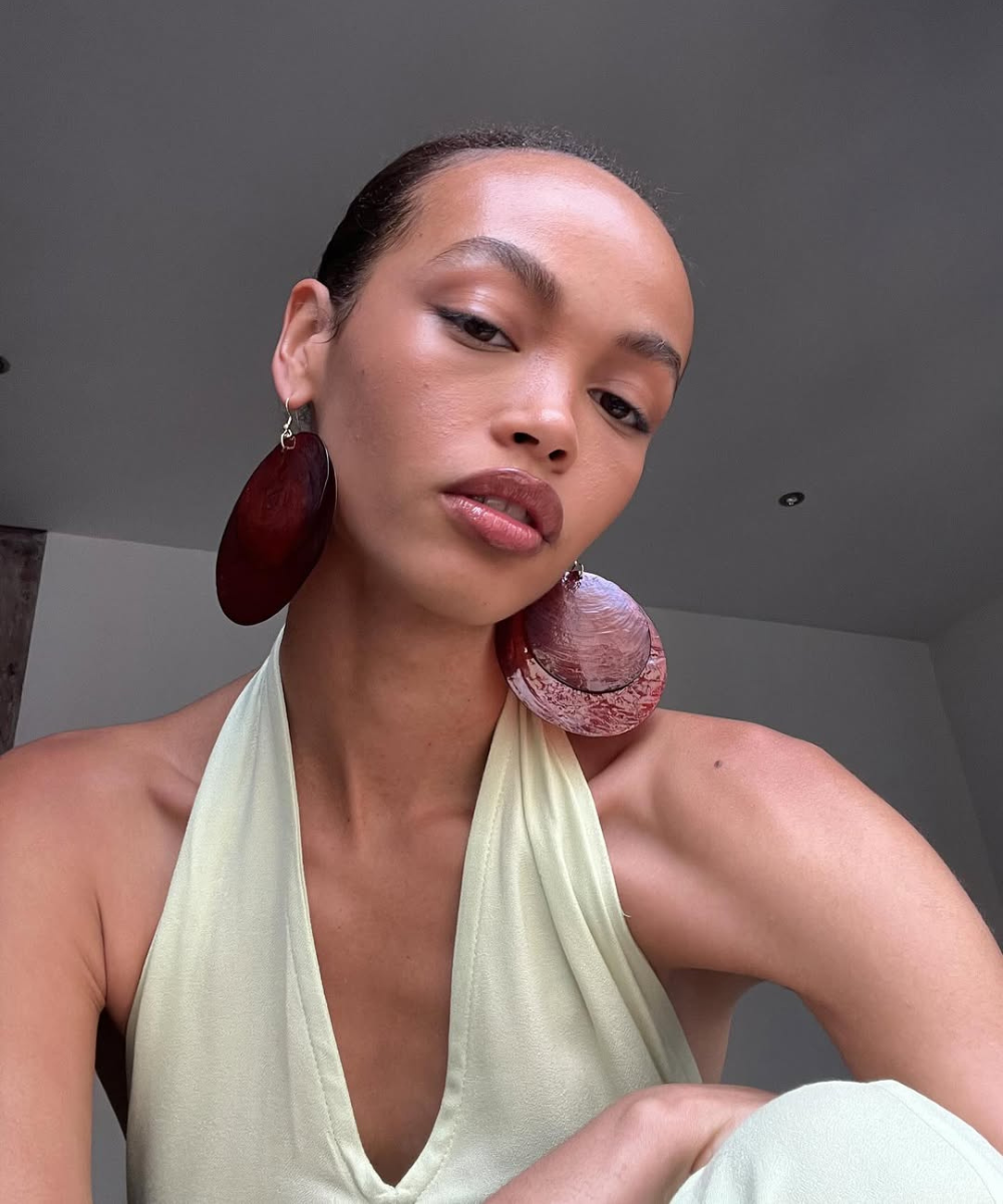 Modelo posa com blusa halter em tecido leve creme e brincos grandes em tom vinho, destacando dicas para ter uma pele bonita