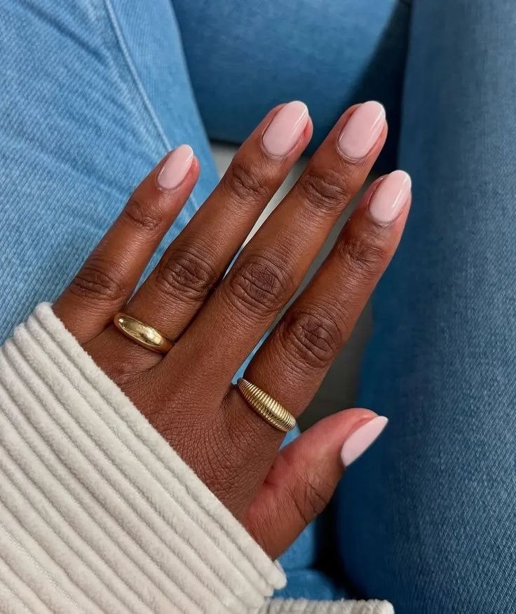Unhas curtas com cores de esmalte 2026 em tom nude rosado brilhoso destacam mãos com anéis dourados sobre jeans azul e