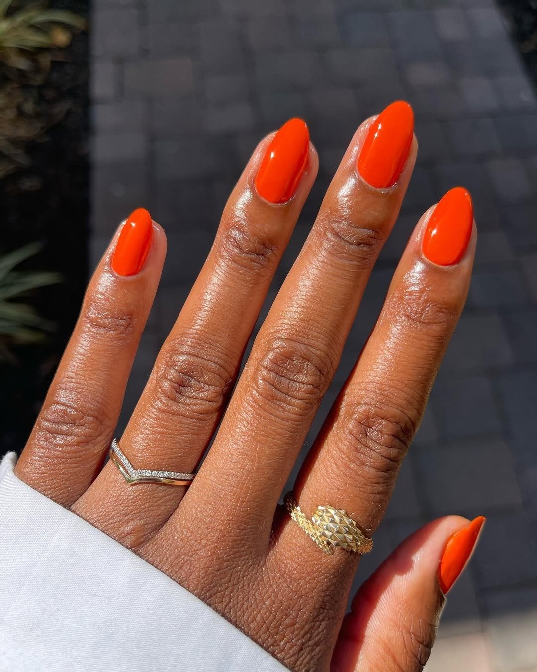 Unhas longas em formato amendoado exibem cores de esmalte 2026 vibrantes em tom laranja intenso com acabamento brilhante,