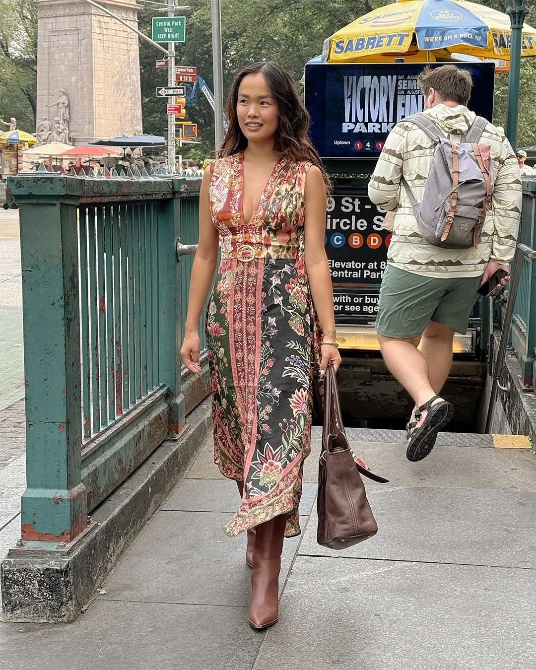 Modelo caminha confiante com vestido Farm Global midi floral patchwork em tons terrosos e botas de couro marrom, carregando