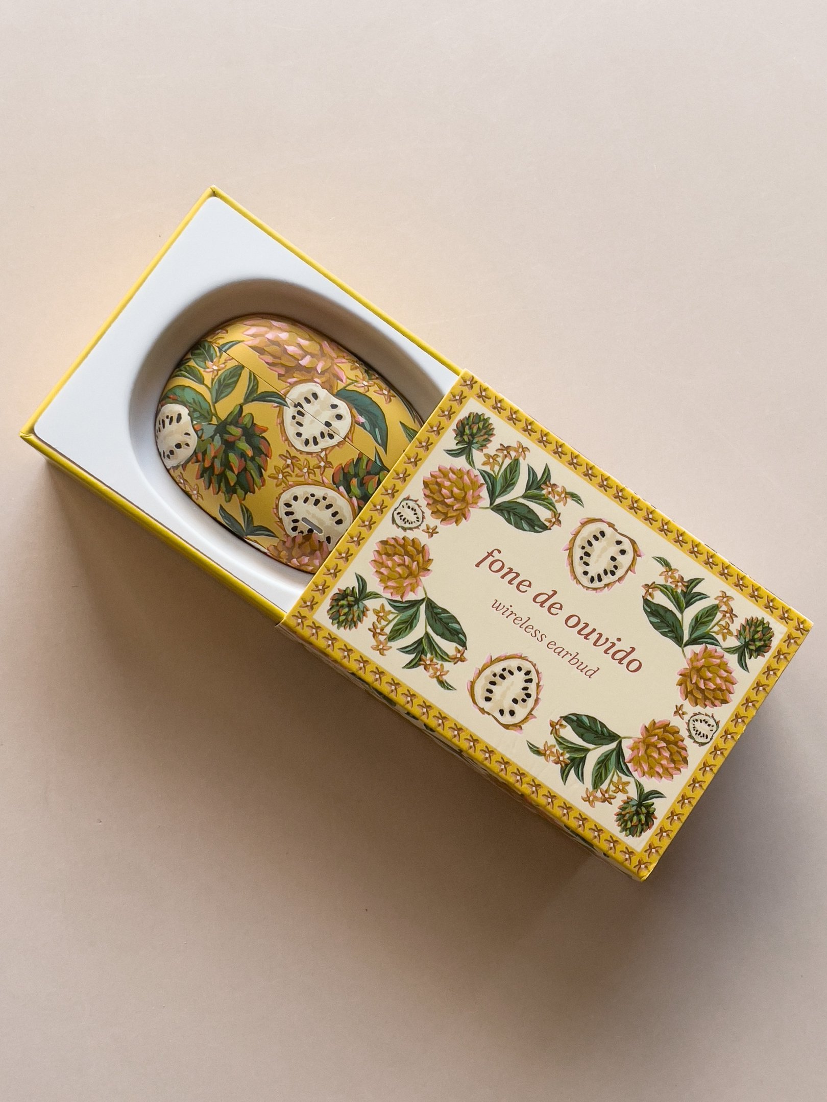 O fone de ouvido da Farm vem em uma embalagem vibrante, com ilustrações florais em tons de amarelo e verde. O design é elegante e reflete a estética da marca, unindo moda e tecnologia.