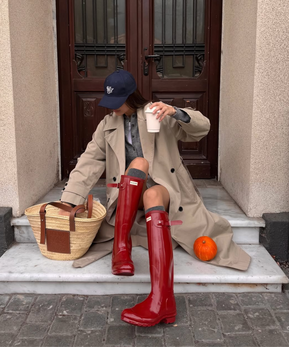 Mulher sentada em uma escada usando um trench coat e bota de chuva bonita. Exemplo de galochas bonitas.